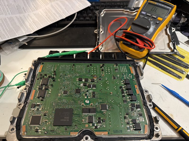 ECU circuit board on workbench with multimeter during automotive electrical diagnostics