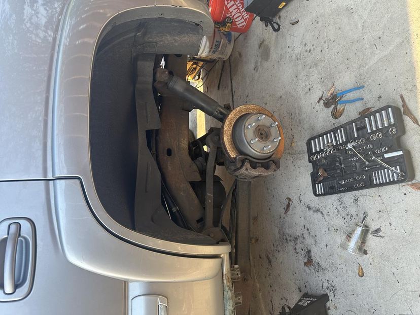 Silver car with the front wheel removed and the hub and knuckle exposed, sockets laid out nearby