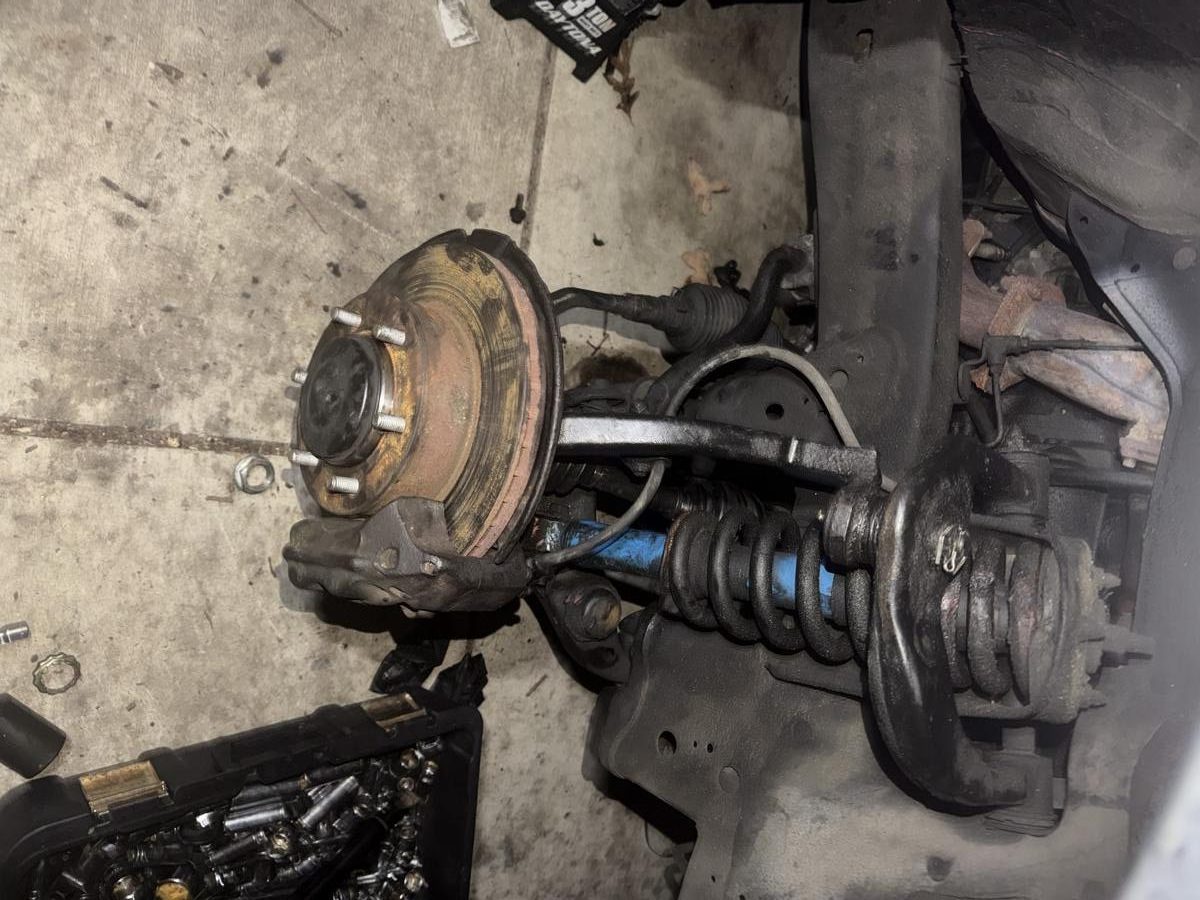 Front hub assembly with strut, coil spring, and brake caliper removed during full suspension overhaul