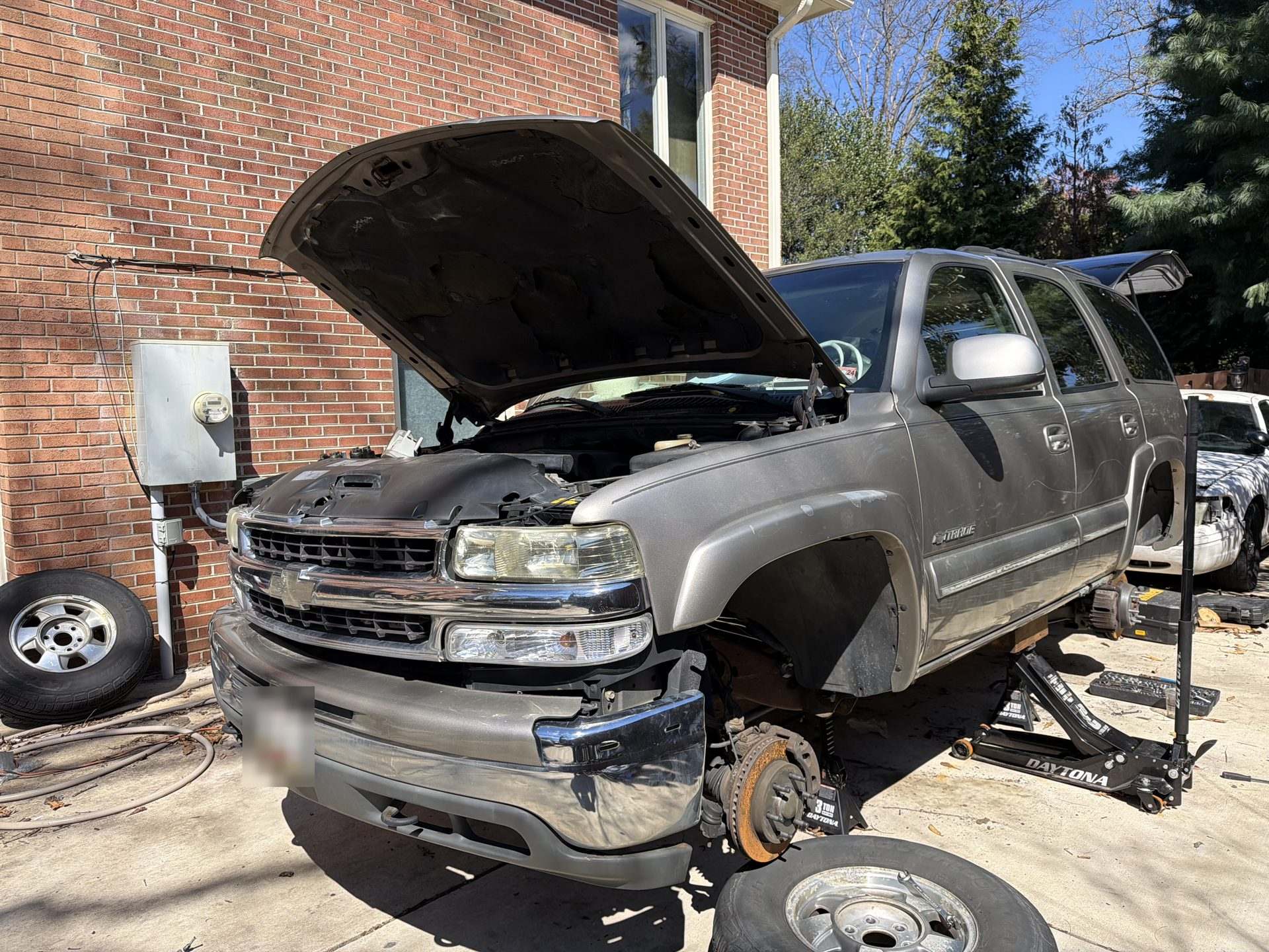 Mobile mechanic service on a Chevrolet SUV in a driveway, hood open and front wheel removed