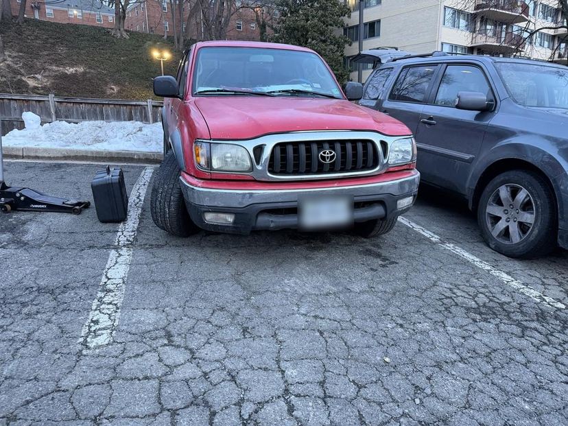 Toyota Tacoma in a parking lot with a floor jack and tool case staged for on-site repair