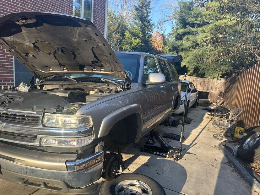 Chevy Tahoe in a driveway with the hood up and a front wheel off on a jack
