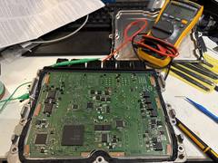 Opened ECU circuit board on a workbench with multimeter probes during electrical diagnostics
