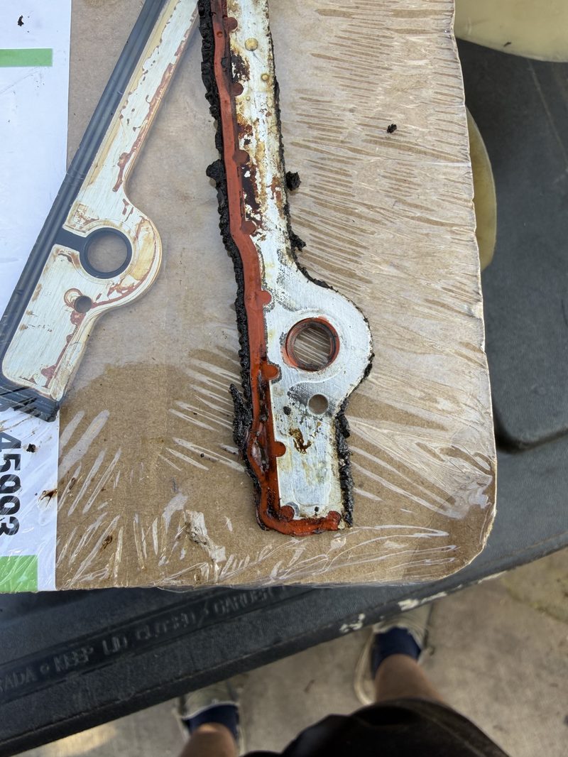 Worn timing cover gasket laid on cardboard for comparison