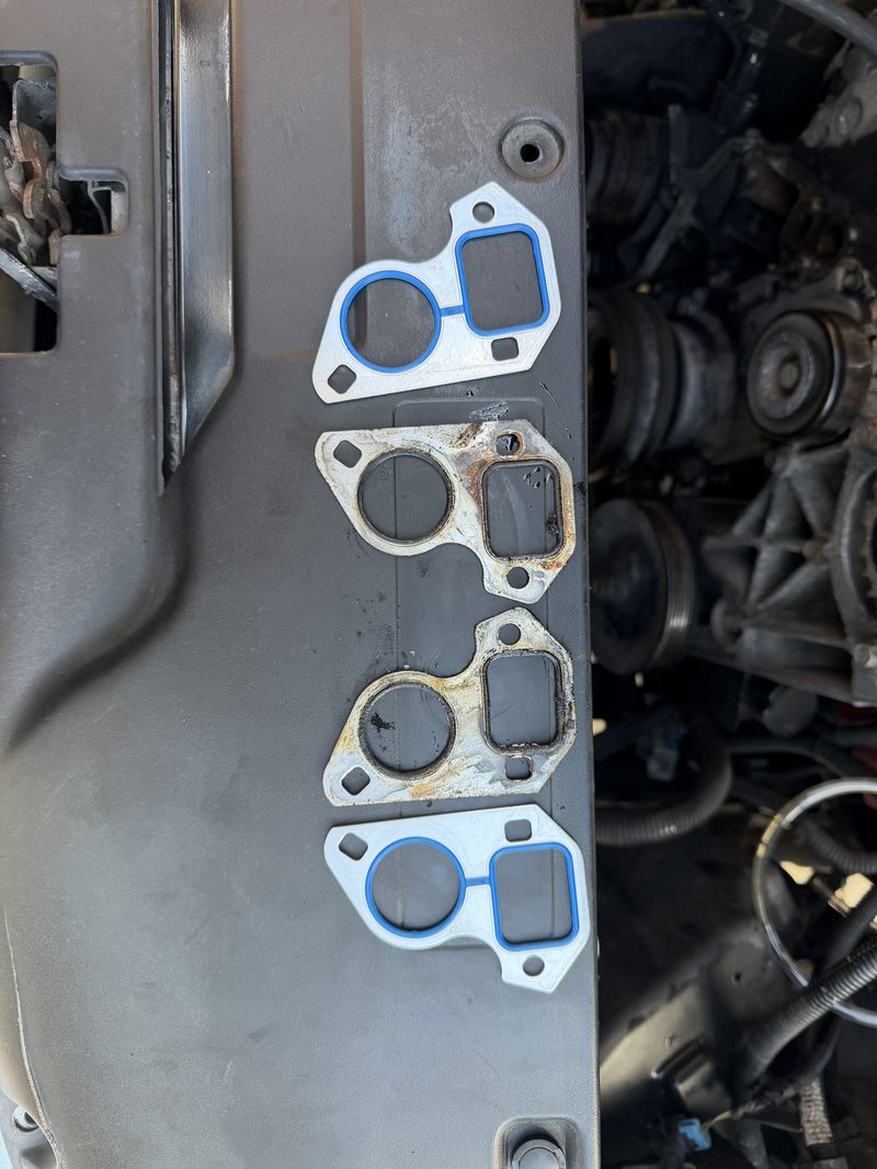 New and old water pump gaskets laid side by side on an engine